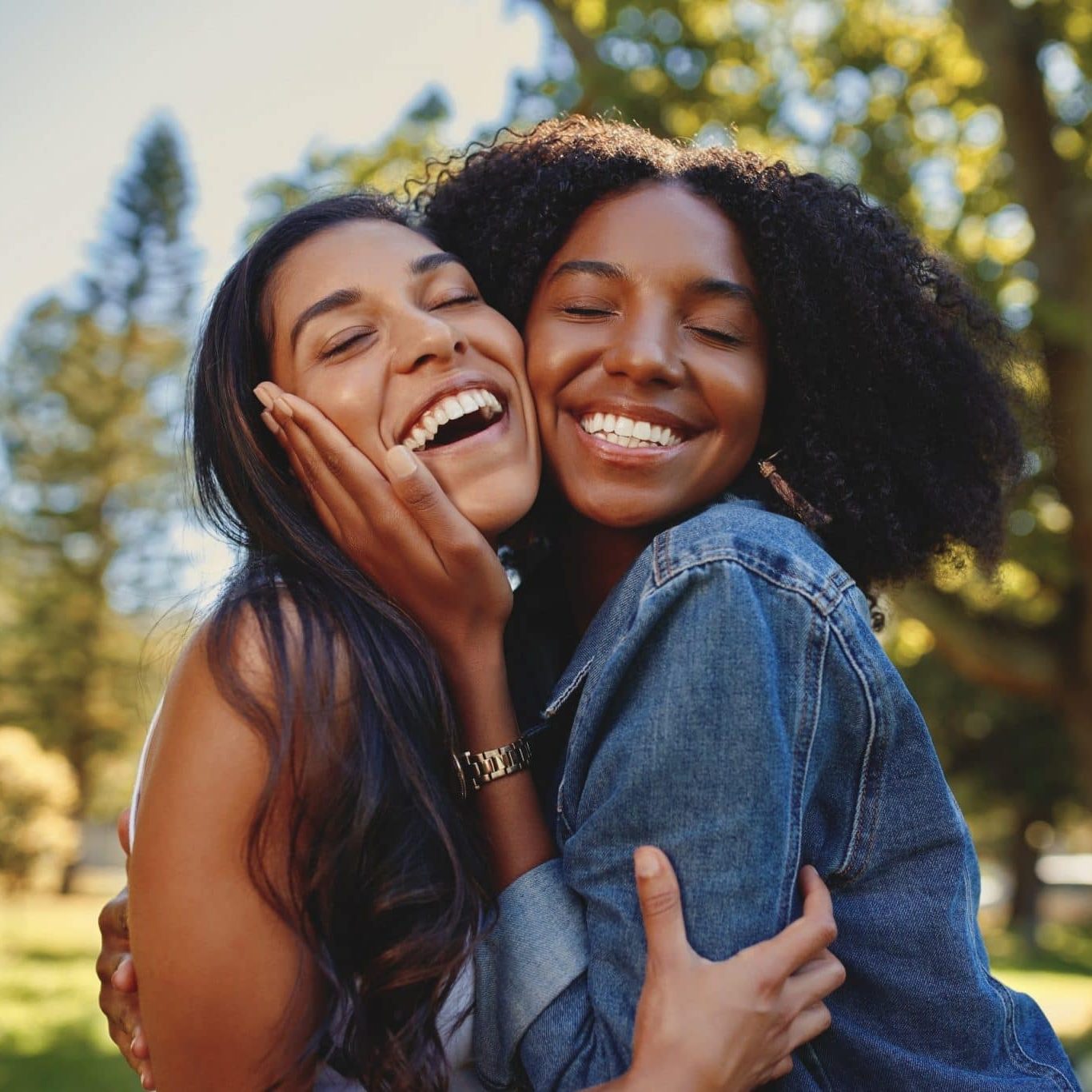 Close up lifestyle portrait of diverse multiracial happy best friends hugging each other and laughing in the park Diverse smiling female friends hugging each other in the park laughing and having fun